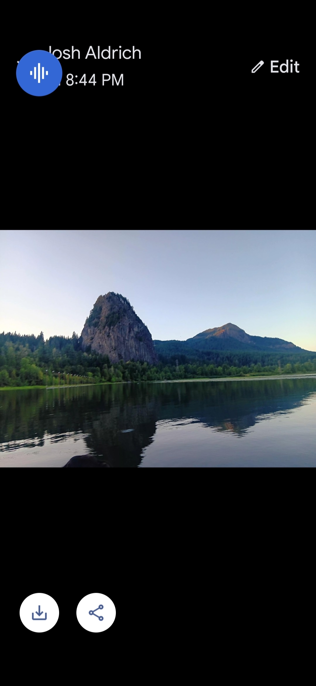 Fotografía amplia de Beacon Rock tomada por Josh Aldrich desde la superficie del Río Columbia mostrando el masivo monolito de basalto que se eleva desde la orilla de Washington con el agua del río reflejando la roca en primer plano y la línea de bosque del Noroeste del Pacífico rodeando la base del monolito