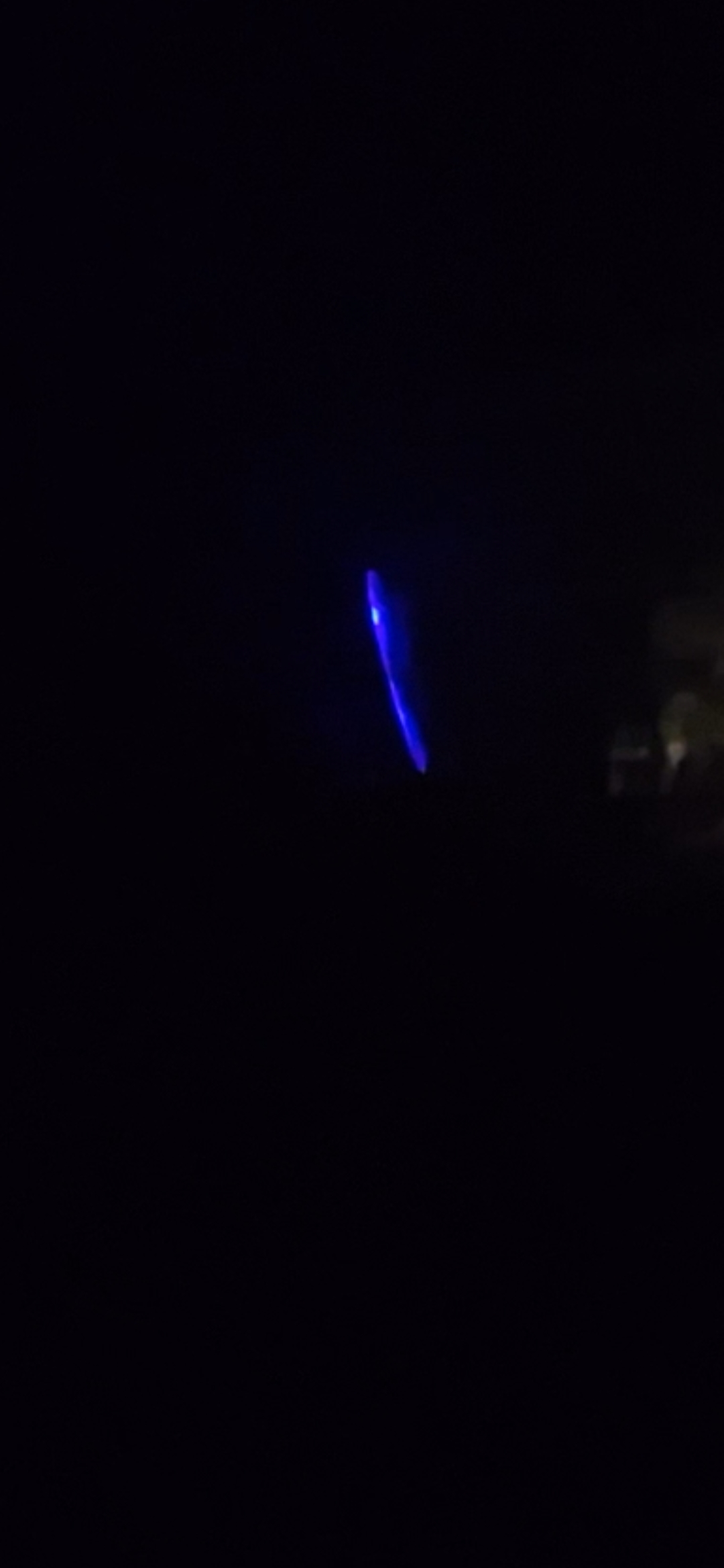 Wide view of the slender blue UAP over Willard Road Stevenson Washington showing the craft at distance in the night sky near the top of the road