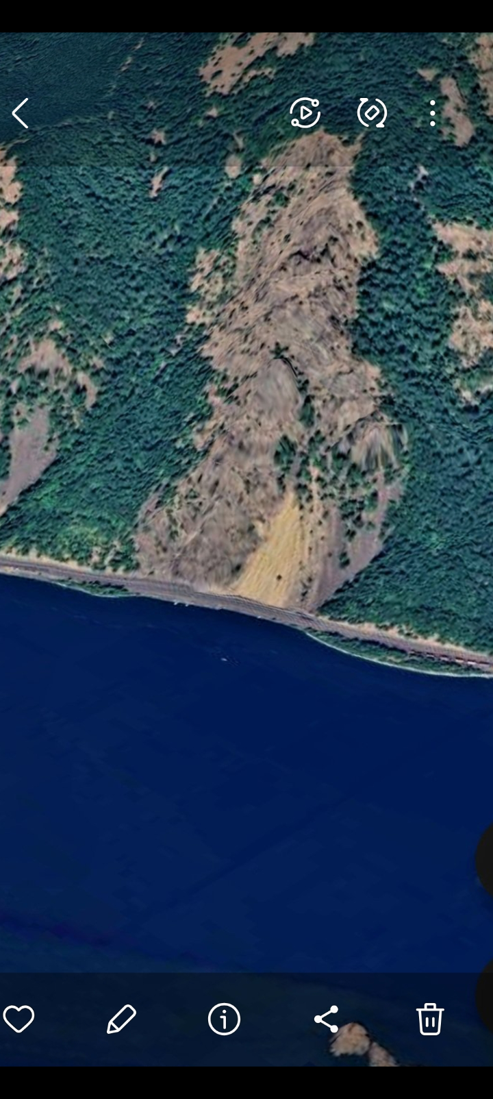 Aerial satellite photograph 2024 of the Washington side of the Columbia River Gorge along Highway 14 showing a distinctive yellow tan exposure on the mountainside above the highway that does not weather like surrounding terrain with the dark blue water of the Columbia River below and the road cutting across the bottom of the frame providing the master context for the underwater USO capture documented in subsequent frames