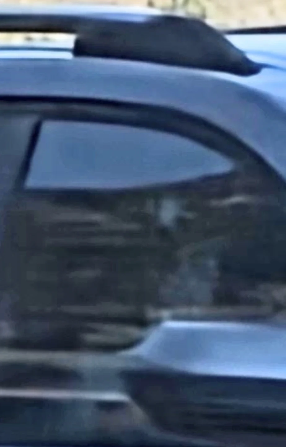 Maximum zoom onto the vehicle occupants confirming reptilian facial geometry through the windshield