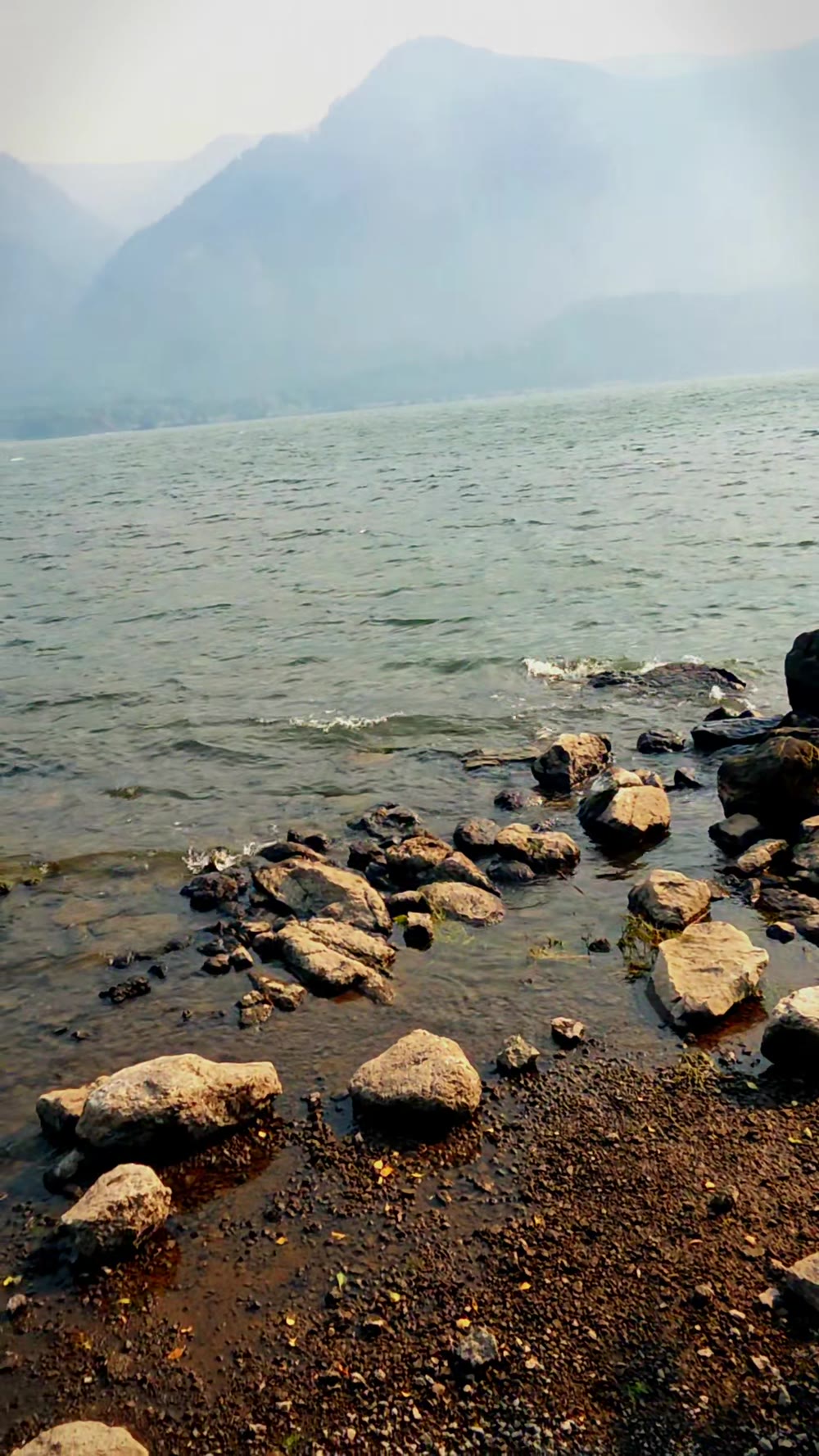 Wide shot of the rocky shoreline at Home Valley Park on the Columbia River, with hazy mountains across the water and wildfire smoke softening the horizon