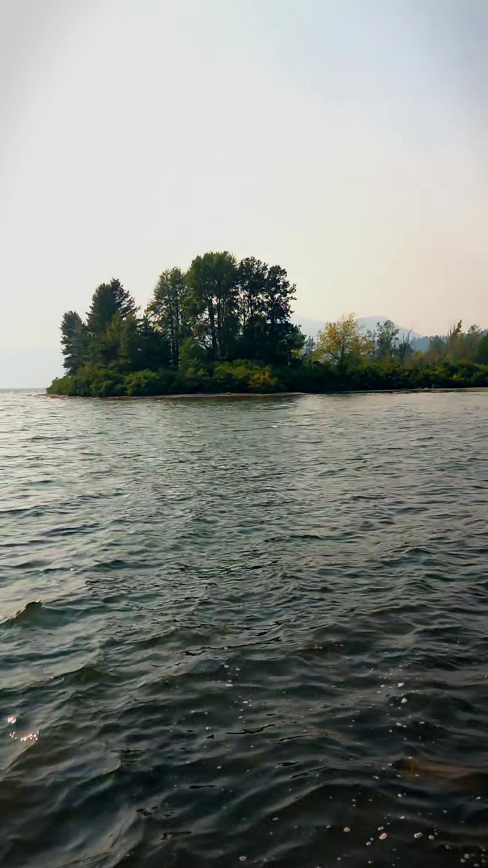 Wide view across the Columbia River channel from Home Valley Park showing the mid-channel water surface and the treeline of the opposite bank in wildfire haze