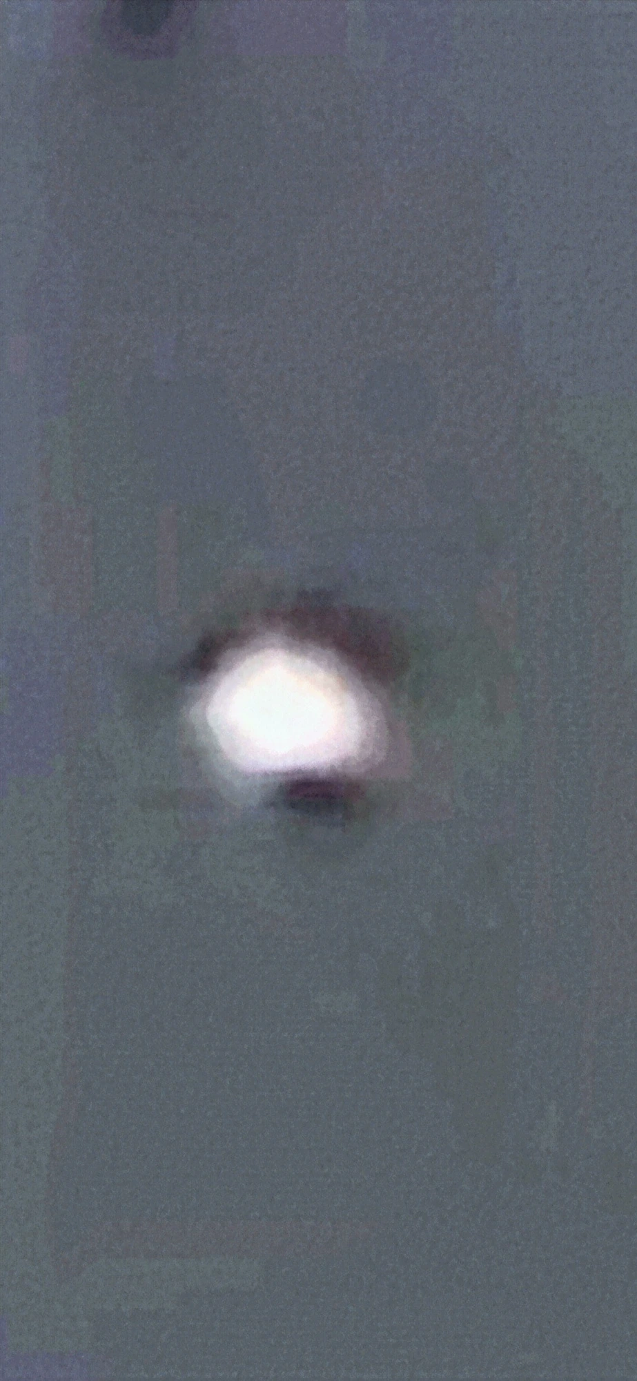 Third zoom frame — the surface anomaly crystallizes: a dark cap-like band appears across the top of the orb, a distinct black oval feature attached at the bottom, and a shadowed curve along the upper-right hemisphere