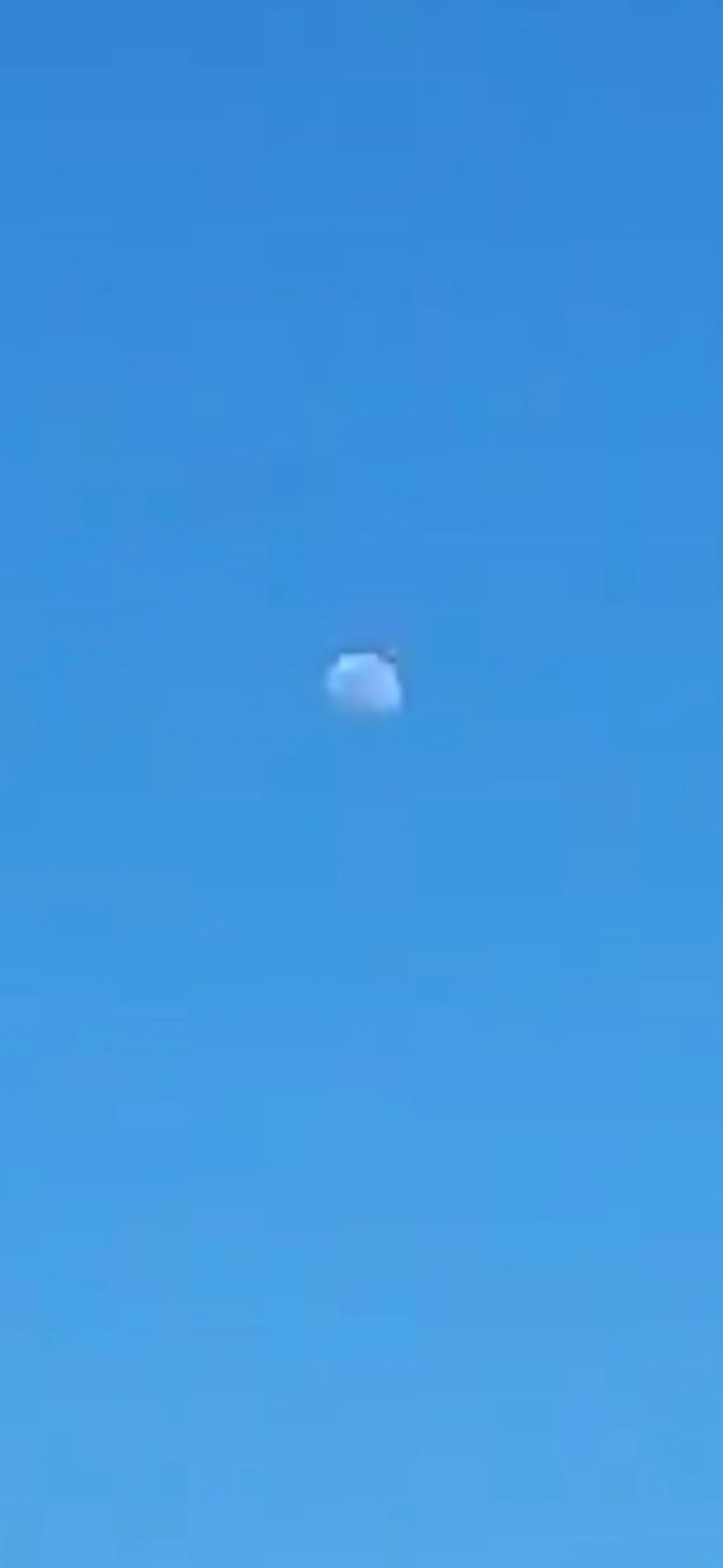 Second environmental context shot showing the luminous white object visible in broad daylight blue sky above a rocky cliff formation demonstrating that the imposter was observable even during daytime when the real moon at that position should not appear this prominent