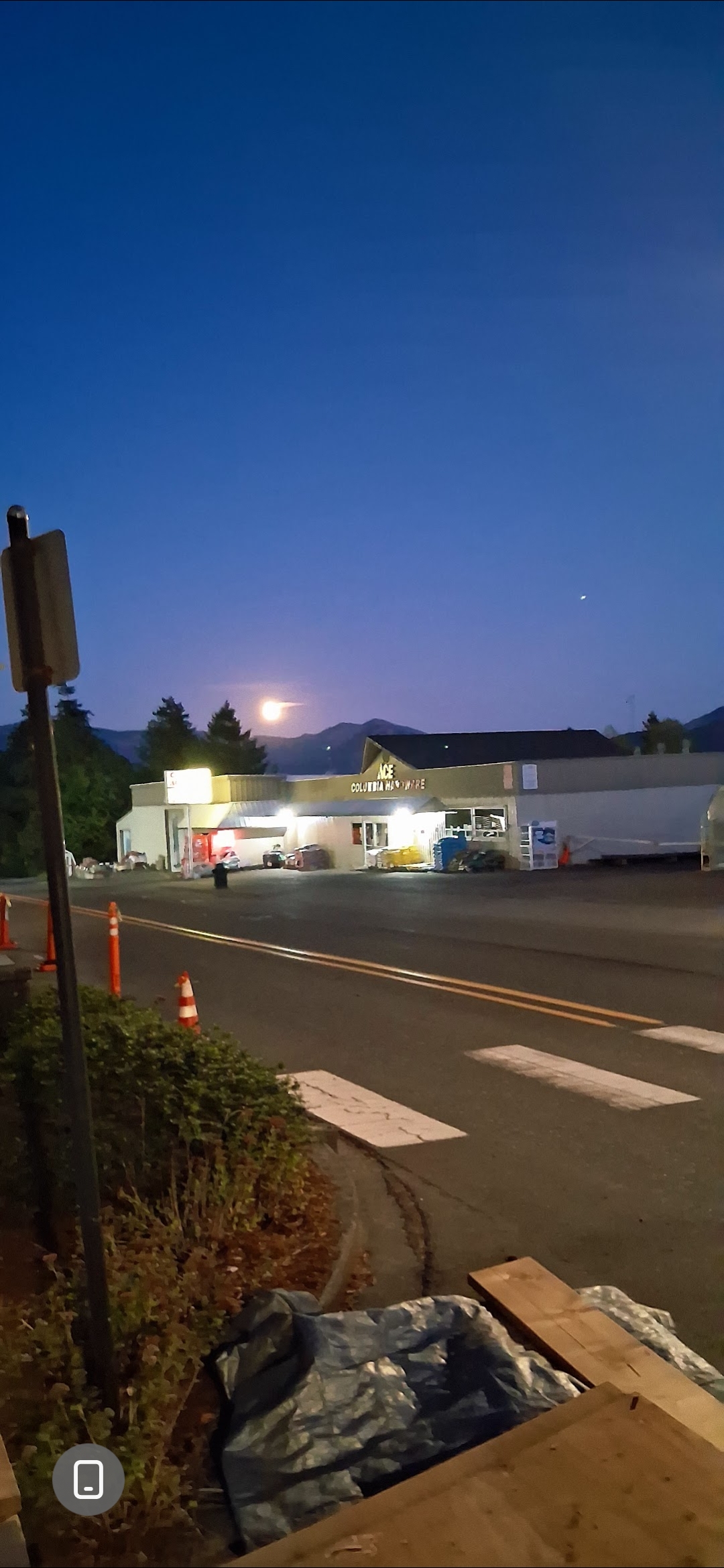 Tercera captura amplia al anochecer desde el estacionamiento del Columbia Ace Hardware en Stevenson Washington mostrando el objeto rectangular oscuro todavía visible contra el cielo crepuscular azul profundo con el comercio completamente iluminado debajo