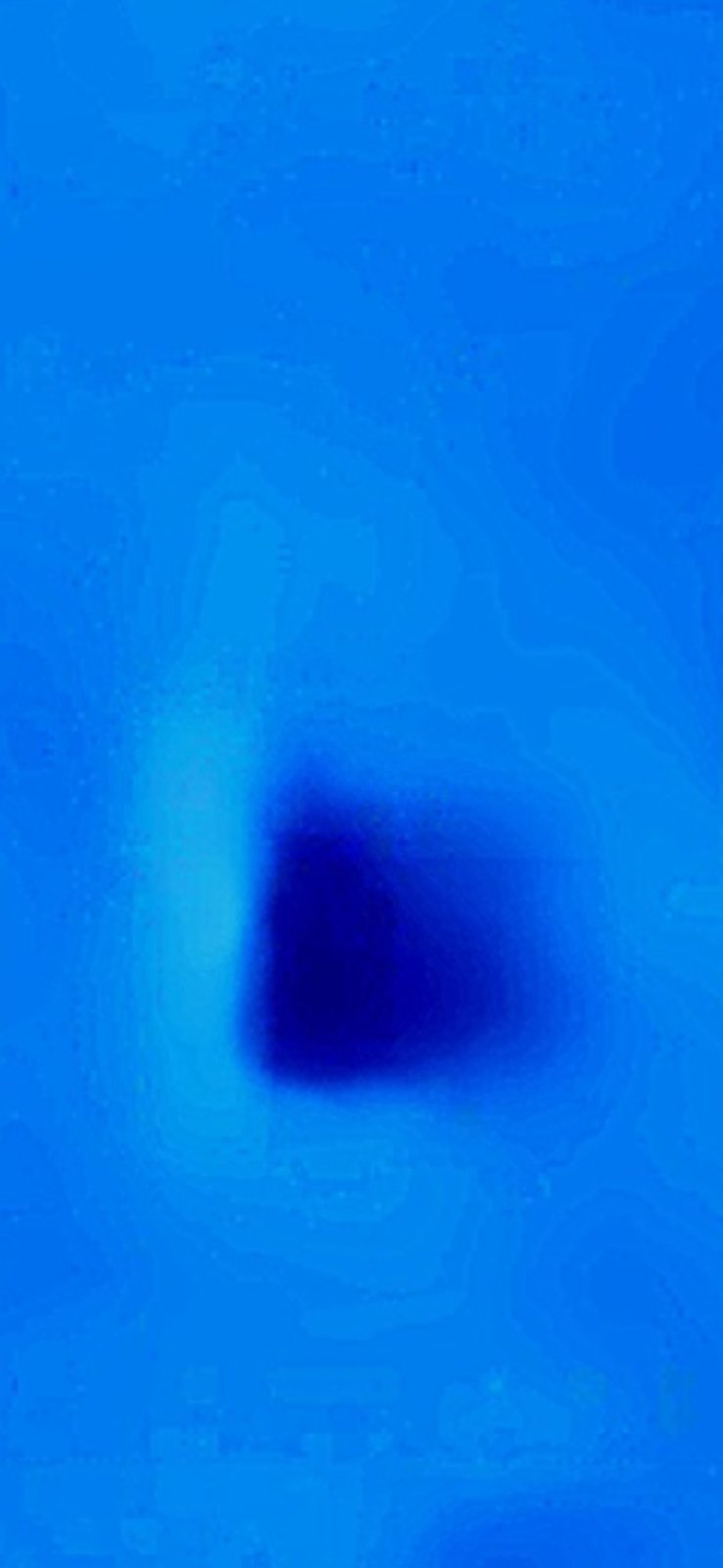 Macro close-up of a single dark teardrop shaped particle isolated against the deep blue Stevenson Washington sky background showing the soft camera-optic edge and the discrete solid-mass interior of one individual dropped object