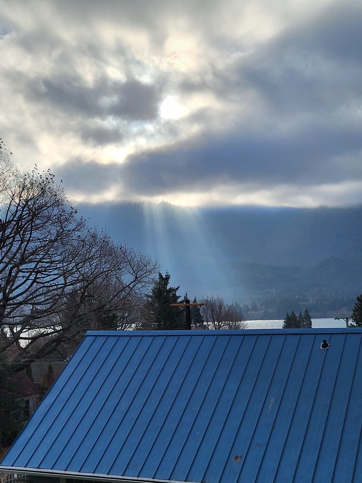 Wide field daytime view from Stevenson Washington looking out over the Columbia River with sun breaking through layered clouds creating multiple distinct crepuscular rays one of which appears to extend all the way to the ground level