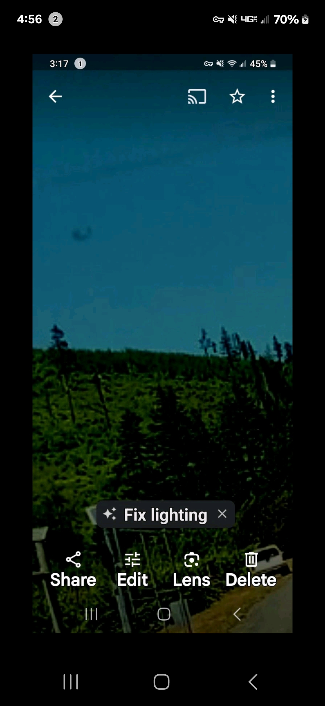 Daytime photograph taken from Kings Rd in Underwood Washington in 2023 showing a dark kettle shaped aerial object suspended above the tree line against an unobstructed blue sky the Perceiver firsthand sighting and personal photograph of the canonical kettle form craft in the air over Underwood Mountain
